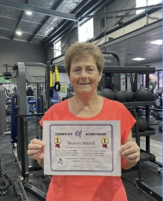 Bronnie holding her certificate of achievement in the gym